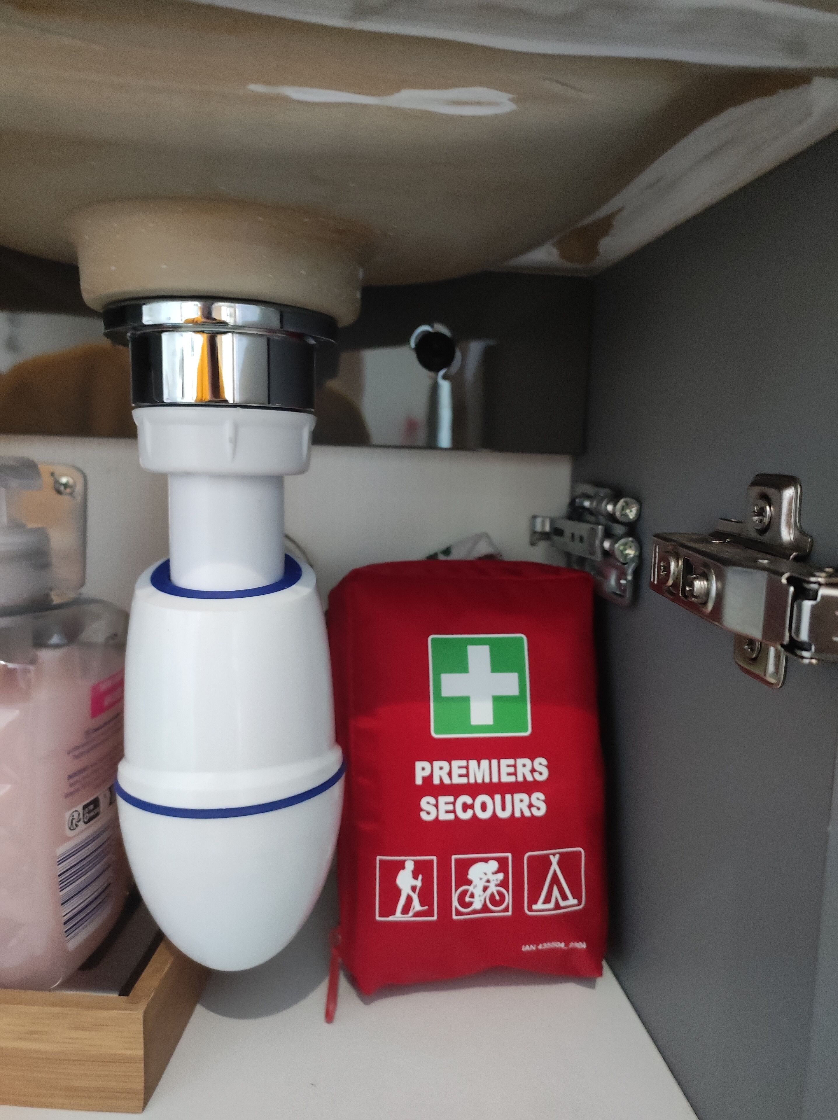 A bathroom sink with a white faucet, a red first aid kit, and a mirror above the sink.