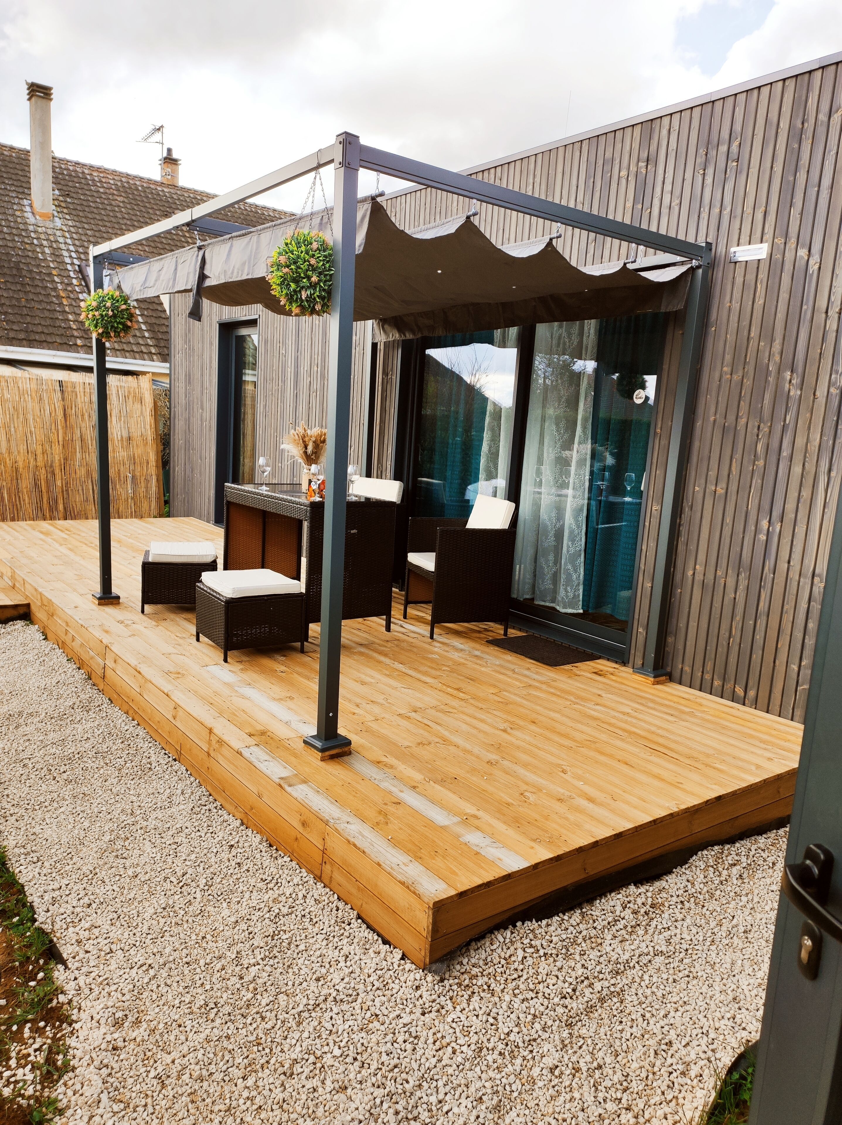 Un espace extérieur aménagé en terrasse, avec un sol en bois, des meubles en osier et une pergola.