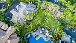 An aerial view of a resort with a swimming pool, palm trees, and resort buildings.