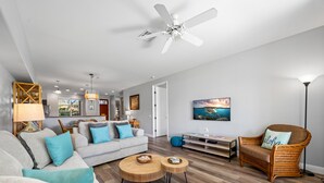 A modern living room with a grey sofa, round wooden coffee tables, a wicker armchair, and a ceiling fan.