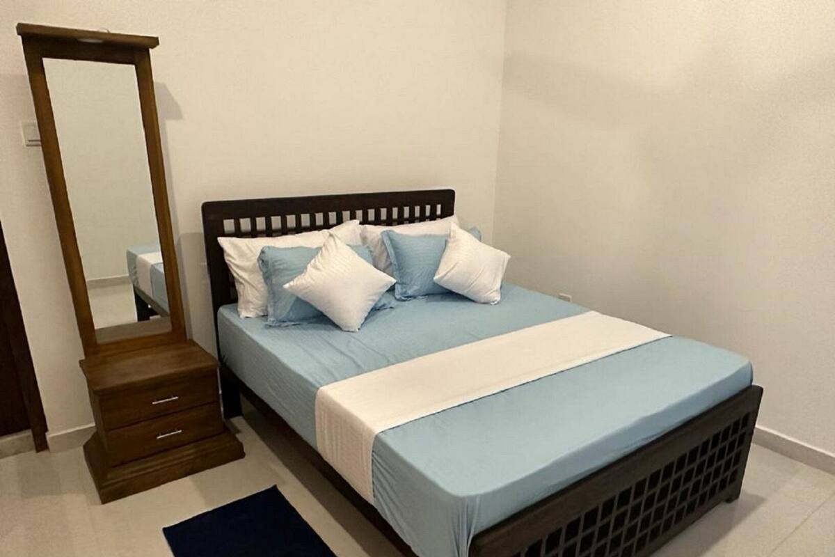 A bedroom with a bed, a dresser, a mirror, and a dark rug.