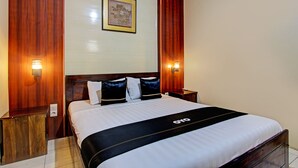 A hotel room with a large bed, wooden headboard, two bedside tables with lamps, and a framed picture on the wall. - Capital O 93533 Griya Denok (Medan)