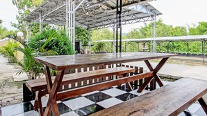 An outdoor covered picnic area with a checkered floor, wooden benches, and a metal roof structure. - Capital O 93533 Griya Denok (Medan)