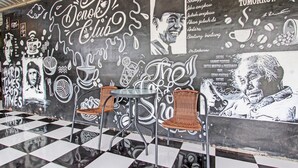 A cafe with a black and white checkered floor, a mural with coffee-related graphics, and wicker chairs. - Capital O 93533 Griya Denok (Medan)
