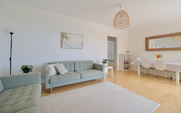 A modern living room with a grey sofa, a white coffee table, and a dining area with a white table and chairs. - Modern Poolside Coogee Beach Sanctuary (Sydney)