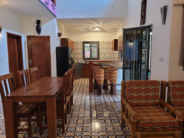 A dining area with a wooden table and chairs, a kitchen with patterned tiles, and a view through a window.