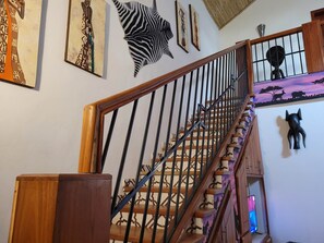 Stunning staircase with artwork-adorned walls and a black sculpture, leading to a cozy landing with a TV and wooden cabinet.
