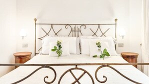 Uma cama com estrutura metálica, roupa de cama branca e duas mesas de cabeceira com abajures.