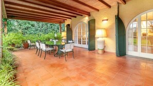 Um pátio externo com piso de azulejos, vigas de madeira e uma mesa com cadeiras.