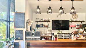 A coffee shop interior with a wooden counter, espresso machines, hanging pendant lights, a chalkboard menu, and a television on the wall. - CHERN CHIANGMAI BOUTIQUE (Chiang Mai)
