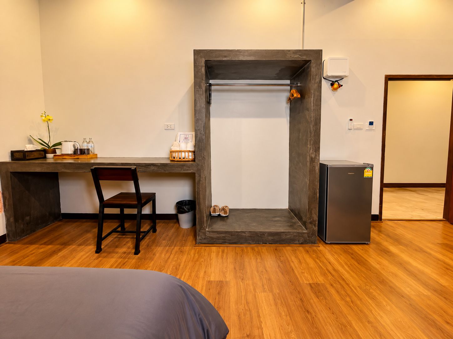 Ein kleines Zimmer mit einem Bett, einem Schreibtisch, einem Stuhl, einem kleinen Kühlschrank und einer Mülleimer.