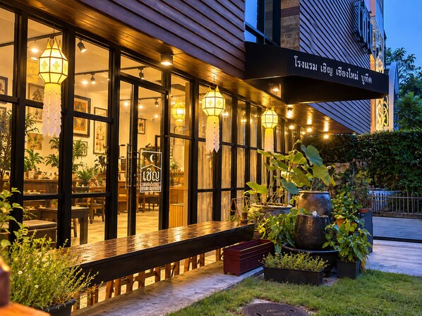 Vista exterior de un restaurante con fachada de madera, ventanas amplias y faroles colgantes.