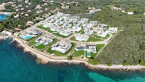 Vista aèria d'una zona residencial costanera amb cases modernes, una marina i aigües turqueses cristal·lines.
