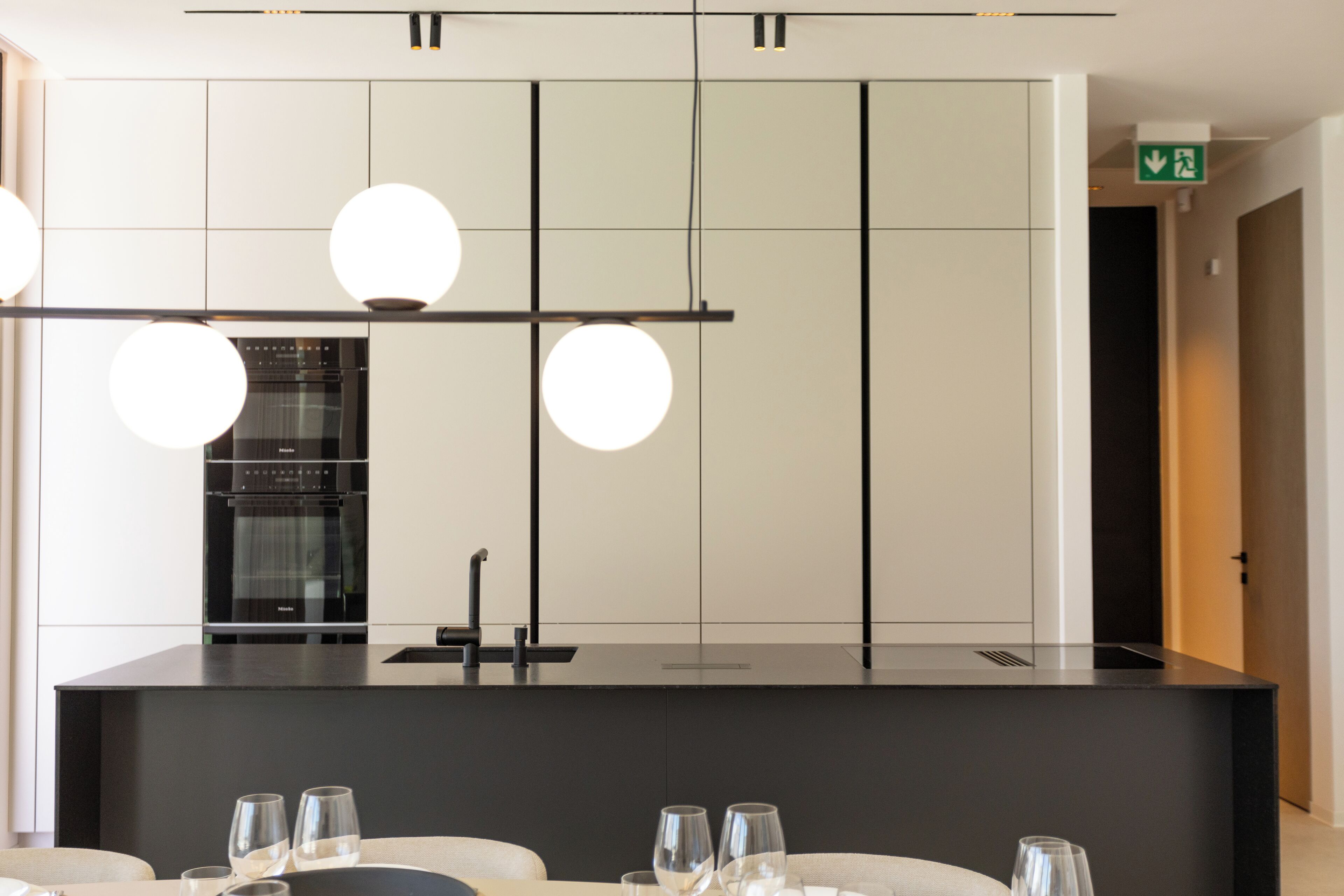 Een moderne keuken met een centraal eiland, hangende verlichting en een inbouwoven.