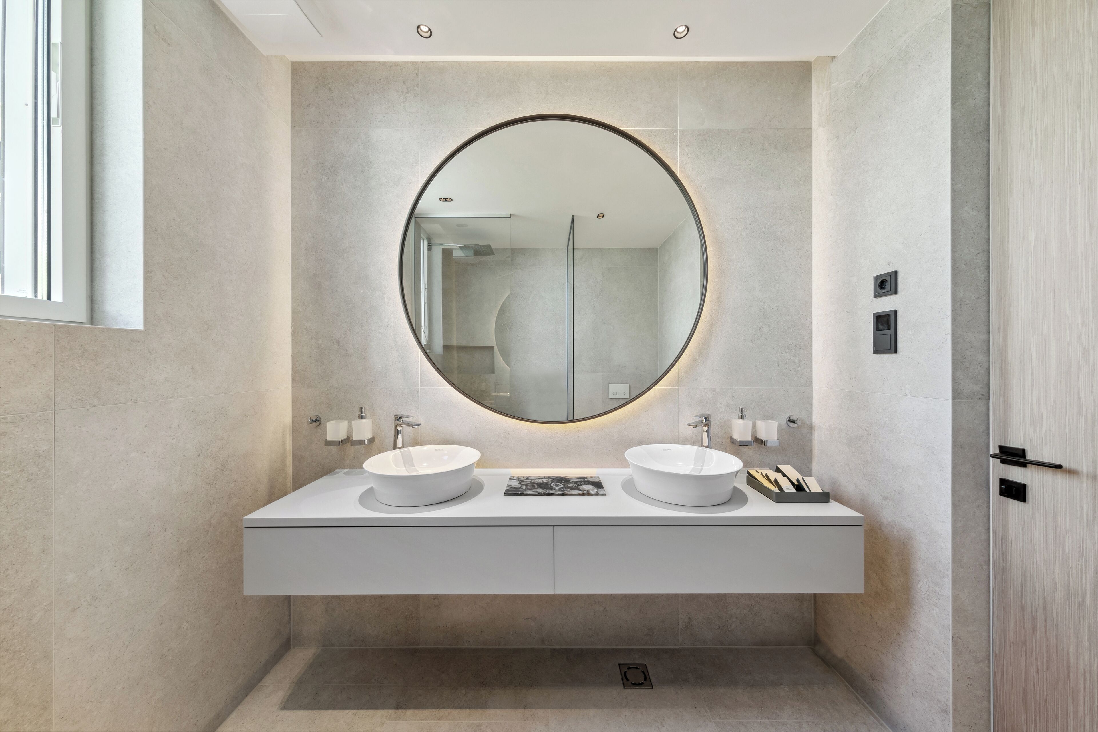 Une salle de bain moderne avec deux lavabos, un grand miroir et un luminaire encastré au plafond.