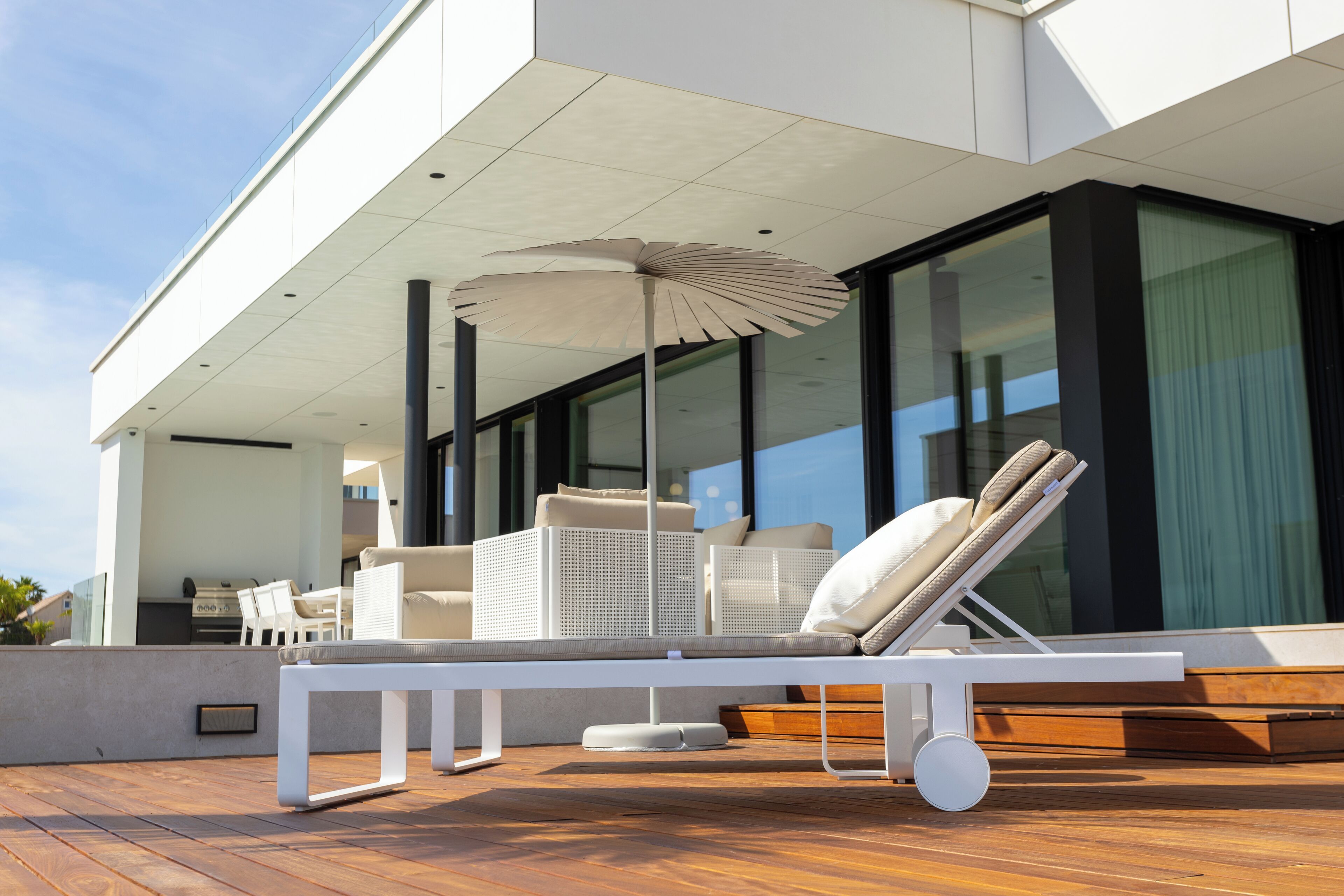 A modern outdoor lounge area with a white table, lounge chairs, and a large umbrella.