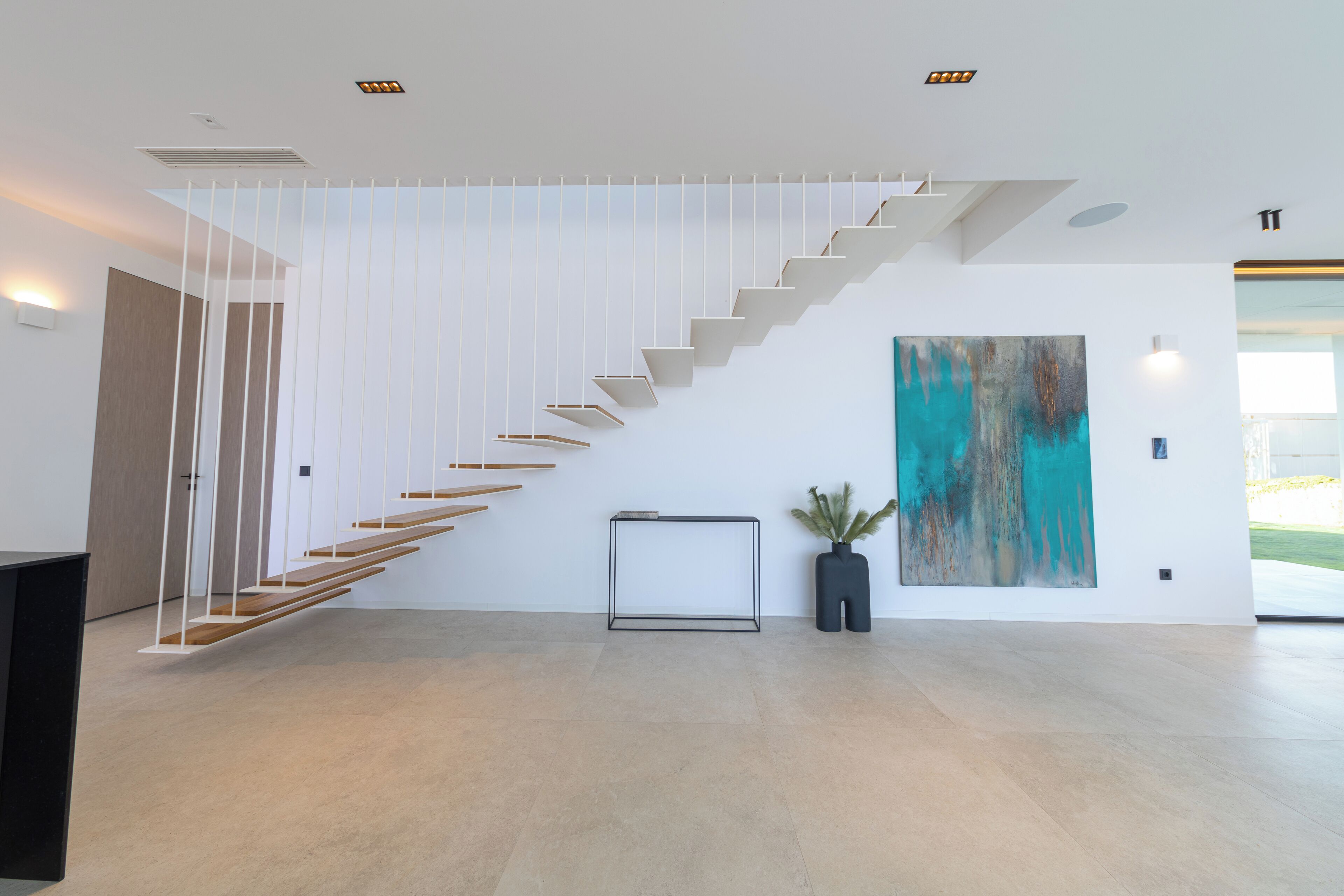A modern interior with a staircase, a minimalist art piece, and a potted plant.