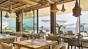 Un restaurant amb taules preparades per a dinar, grans finestres i llums penjants.