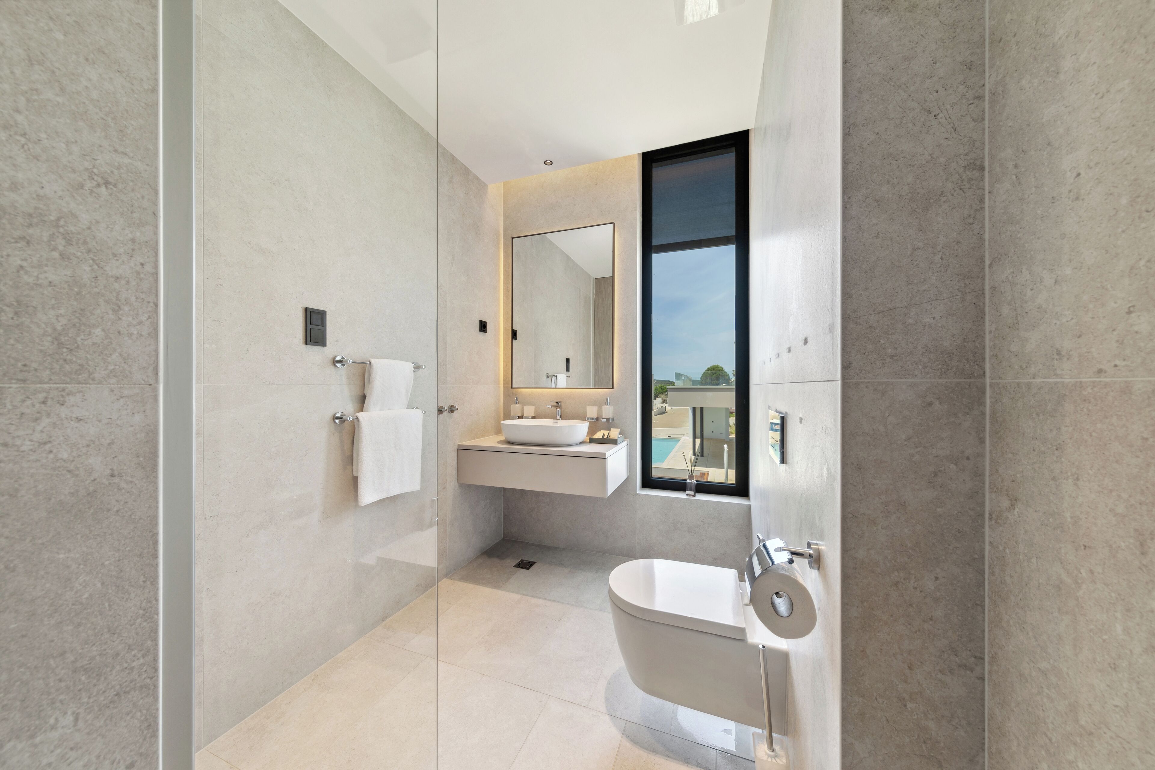 A modern bathroom with a glass shower enclosure, a freestanding toilet, a vanity with a sink, and a large mirror.