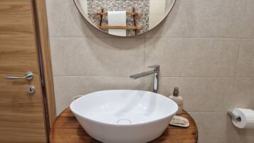 A bathroom with a round wooden vanity, a white sink, a mirror, and a towel hanging on the door.