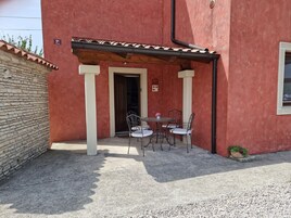 Un edificio de fachada roja, techo de tejas y un pequeño patio con mesa y sillas.