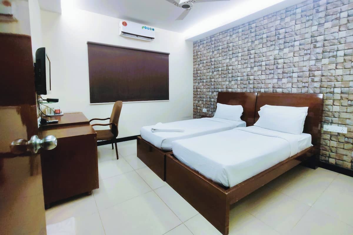 Quarto de hotel com duas camas, uma escrivaninha, uma cadeira, uma televisão e um ventilador de teto.