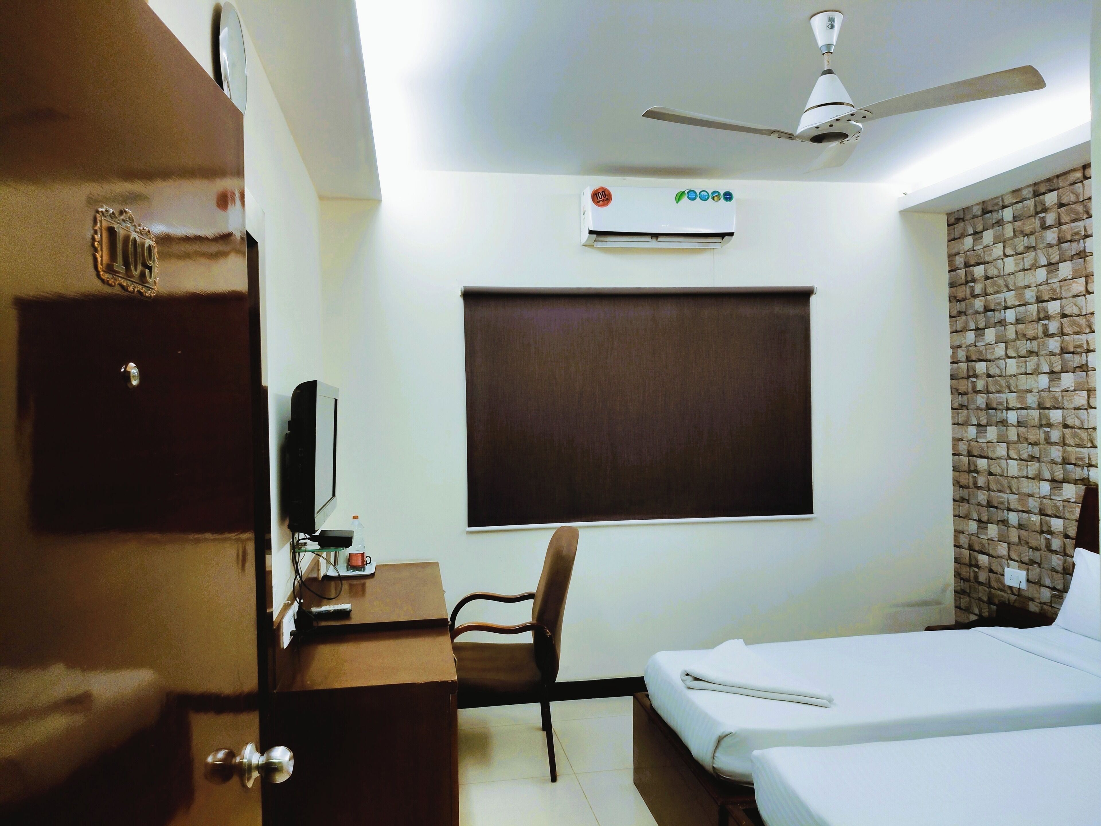 A hotel room with a bed, a desk, a chair, a television, an air conditioner, and a ceiling fan.