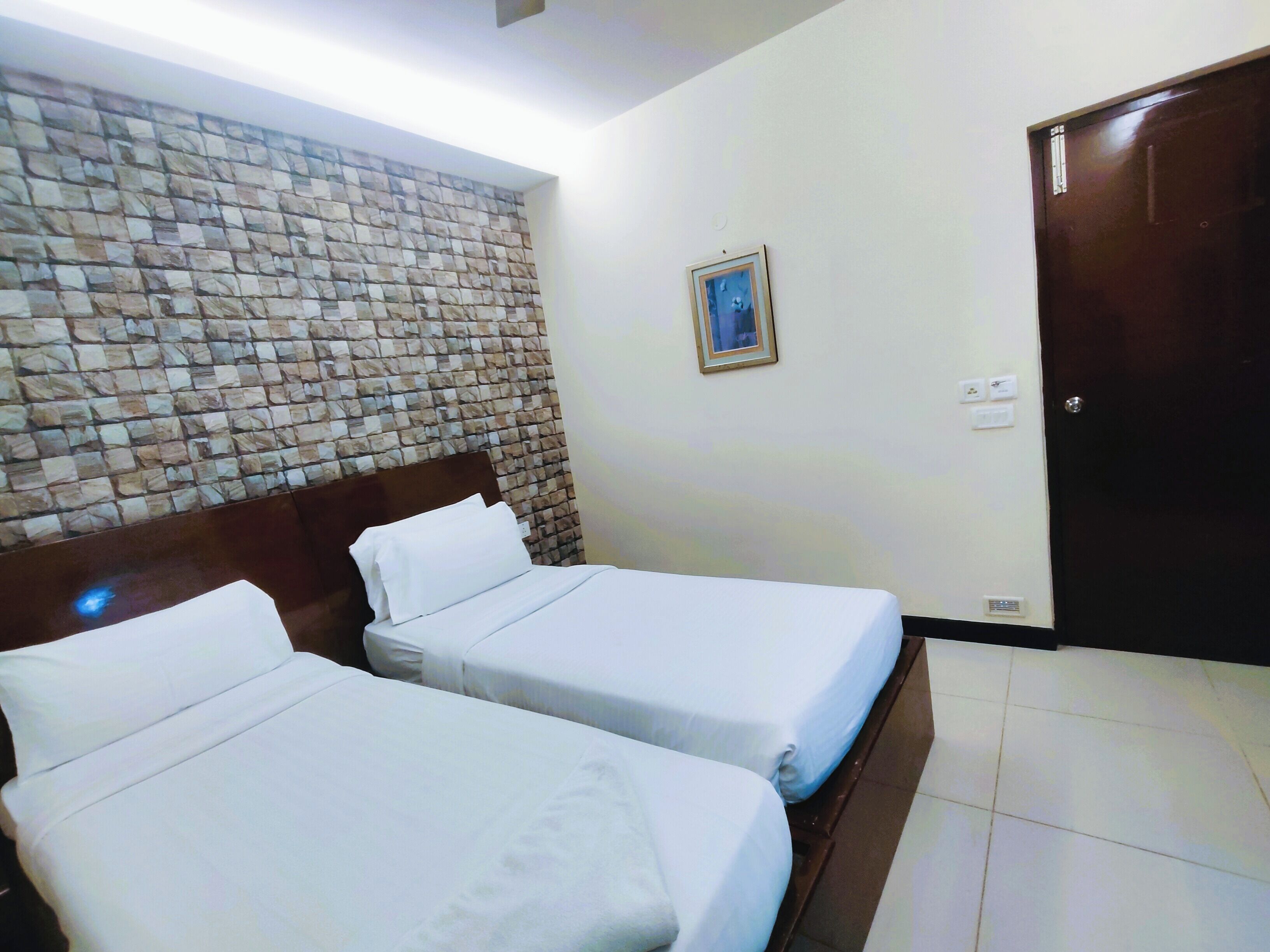 Habitación de hotel con dos camas, pared con diseño de piedra, un cuadro enmarcado y una puerta.