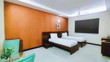 A hotel room with two single beds, a desk, a chair, a small table with a plant, and a large window.