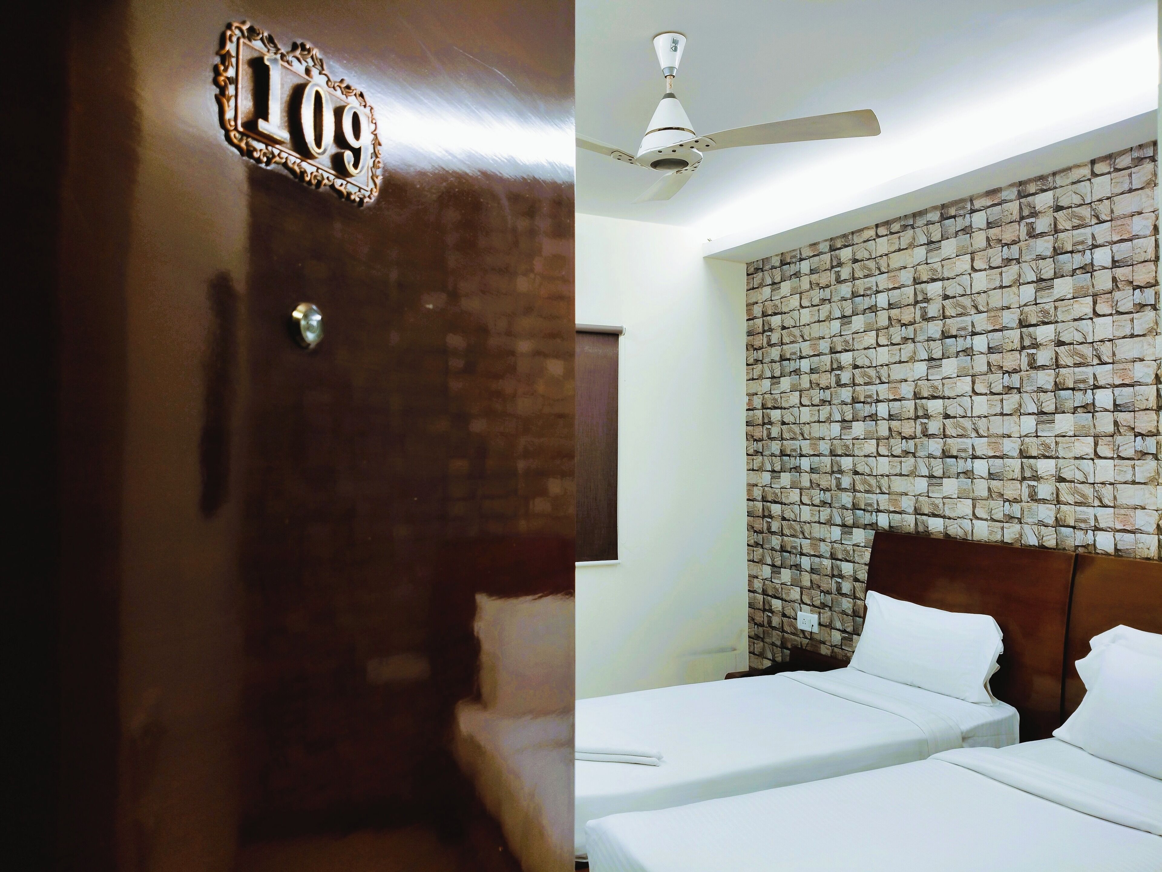 A hotel room with a brick wall, a ceiling fan, and two beds.