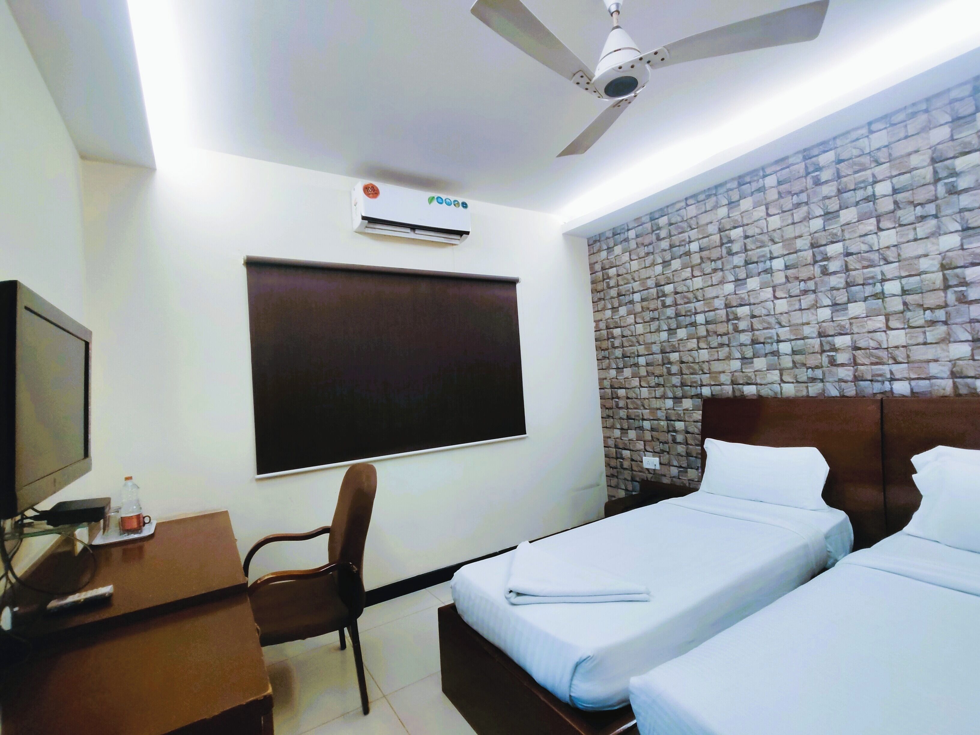 A hotel room with a bed, a desk, a chair, a television, an air conditioner, and a ceiling fan.