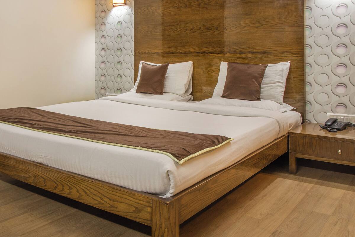 Cama bem arrumada com estrutura de madeira, manta marrom e dois travesseiros.