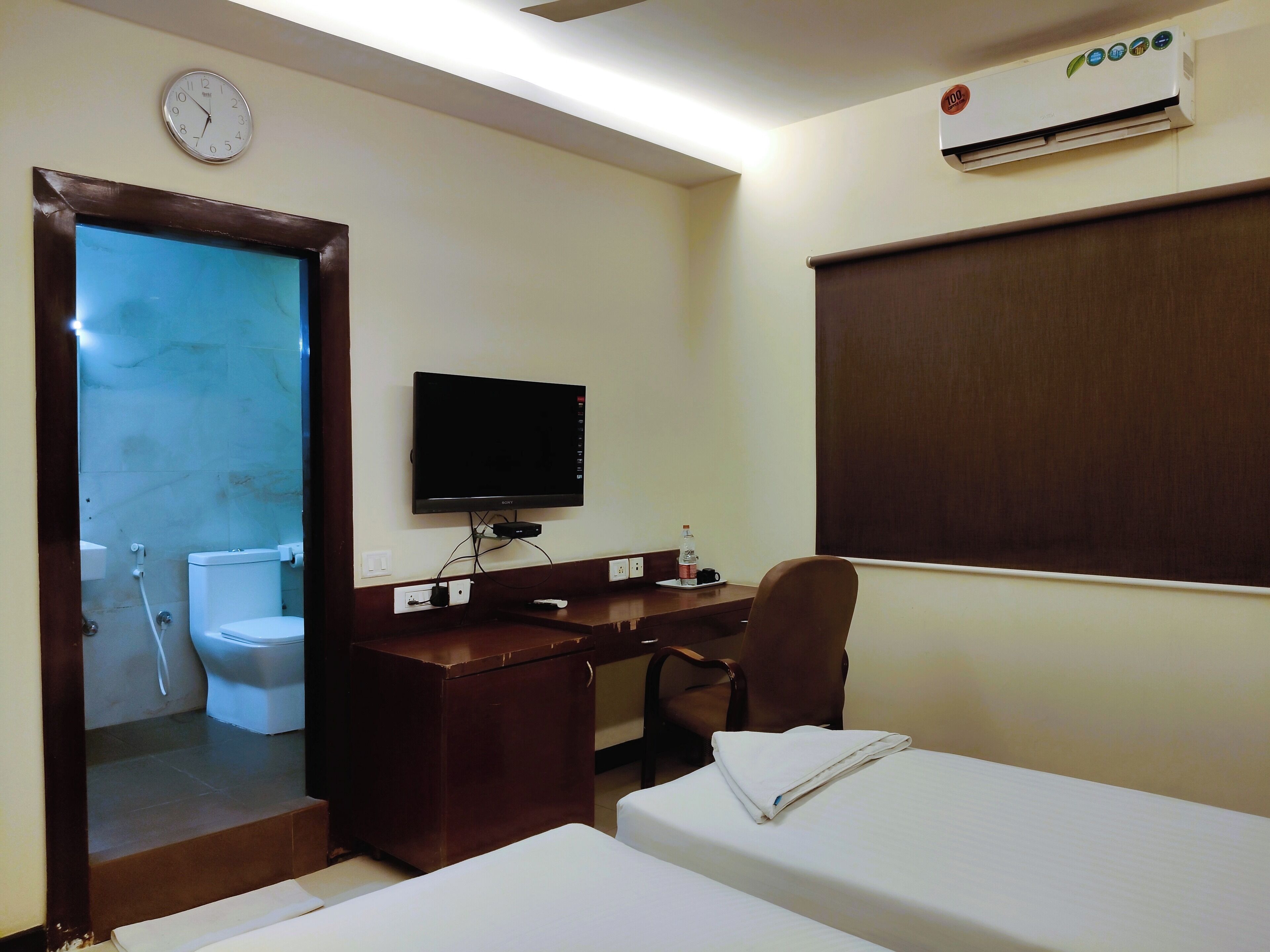Een hotelkamer met een bed, een bureau, een televisie, een wekker en een airconditioner.