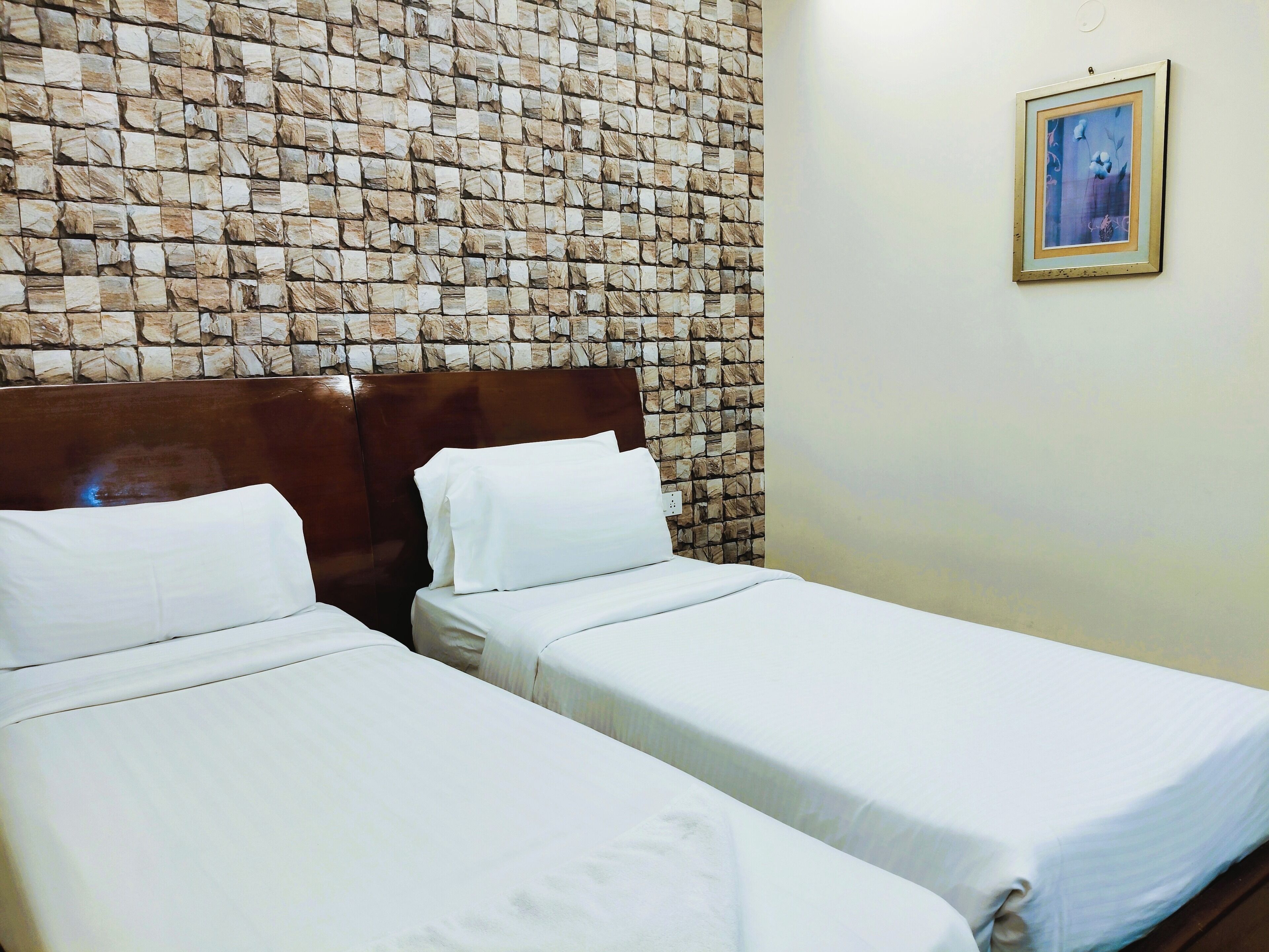 A room with two beds, a wooden headboard, a stone-patterned wall, and a framed picture on the wall.