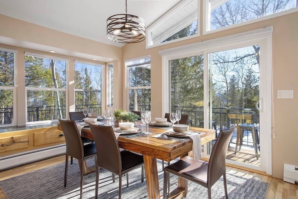 Comedor con una mesa de madera dispuesta para cuatro personas, sillas, ventanas amplias y vistas a árboles.