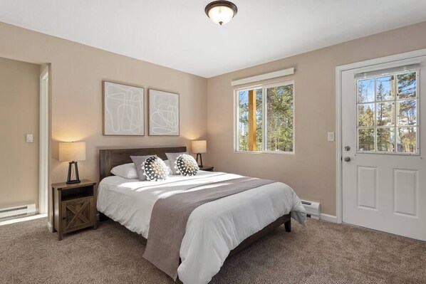 A bedroom with a bed, bedside lamps, a door, and a window.