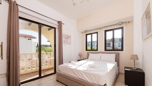 A bedroom with a bed, a nightstand, a window, and a sliding glass door leading to a balcony. - Villa Artemis (Paralimni)