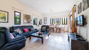 A spacious living room with a black leather sofa, a glass coffee table, and a dining area with a wooden table and chairs. - Villa Artemis (Paralimni)