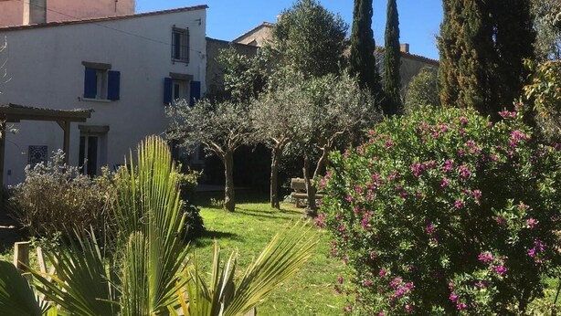 Ein Garten mit einem weißen Gebäude, grünem Rasen und blühenden Büschen.