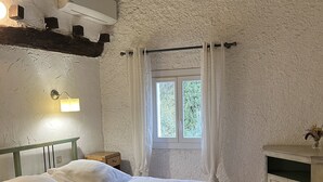 Ein Schlafzimmer mit Bett, Nachttisch, Kommode, einem Fenster mit Vorhängen und einer Wand-Klimaanlage.