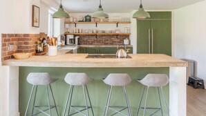 Une cuisine dotée d’un îlot central vert, de tabourets de bar, de luminaires suspendus et d’un mur de fond en briques.