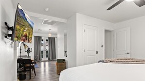 Moderni hotellihuone, jossa on suuri sänky, työpöytä tietokoneella, seinälle asennettu televisio ja kattotuuletin.