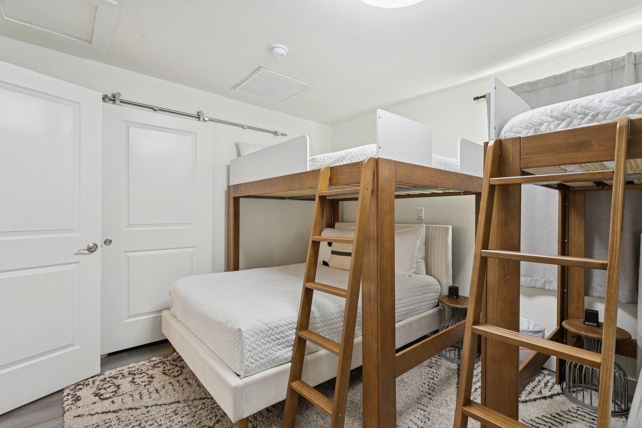 Quarto com beliche, uma escada, porta branca e uma mesinha de cabeceira.