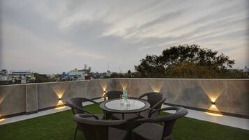 A rooftop terrace with a round table and wicker chairs, surrounded by artificial grass.