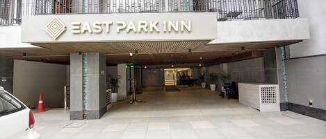 La entrada al East Park Inn, con un letrero llamativo, un corredor cubierto y un mostrador de recepción.