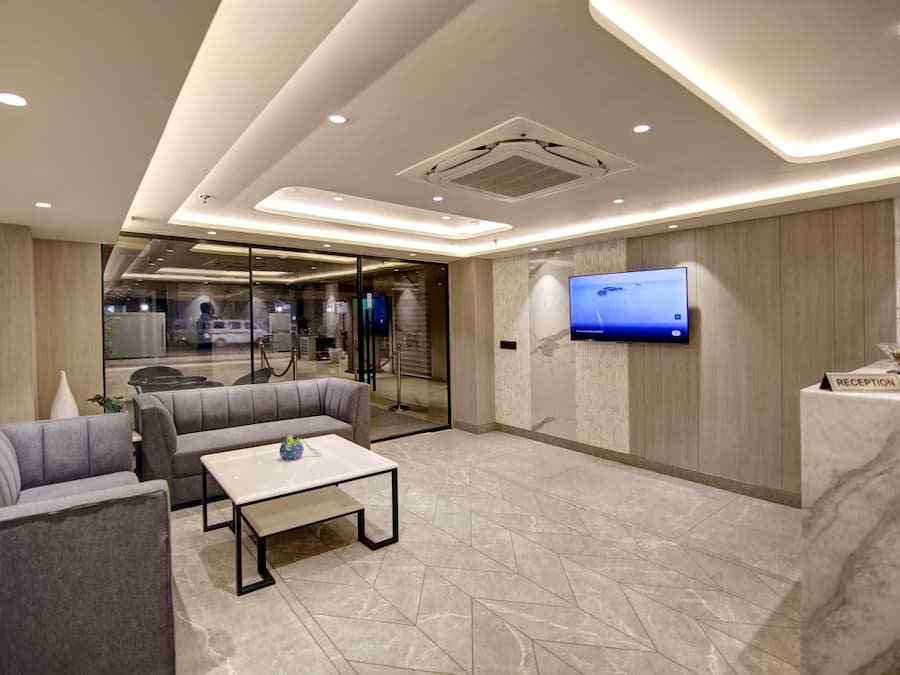 A modern lobby with a reception desk, a flat-screen TV, and a seating area with sofas and a coffee table.