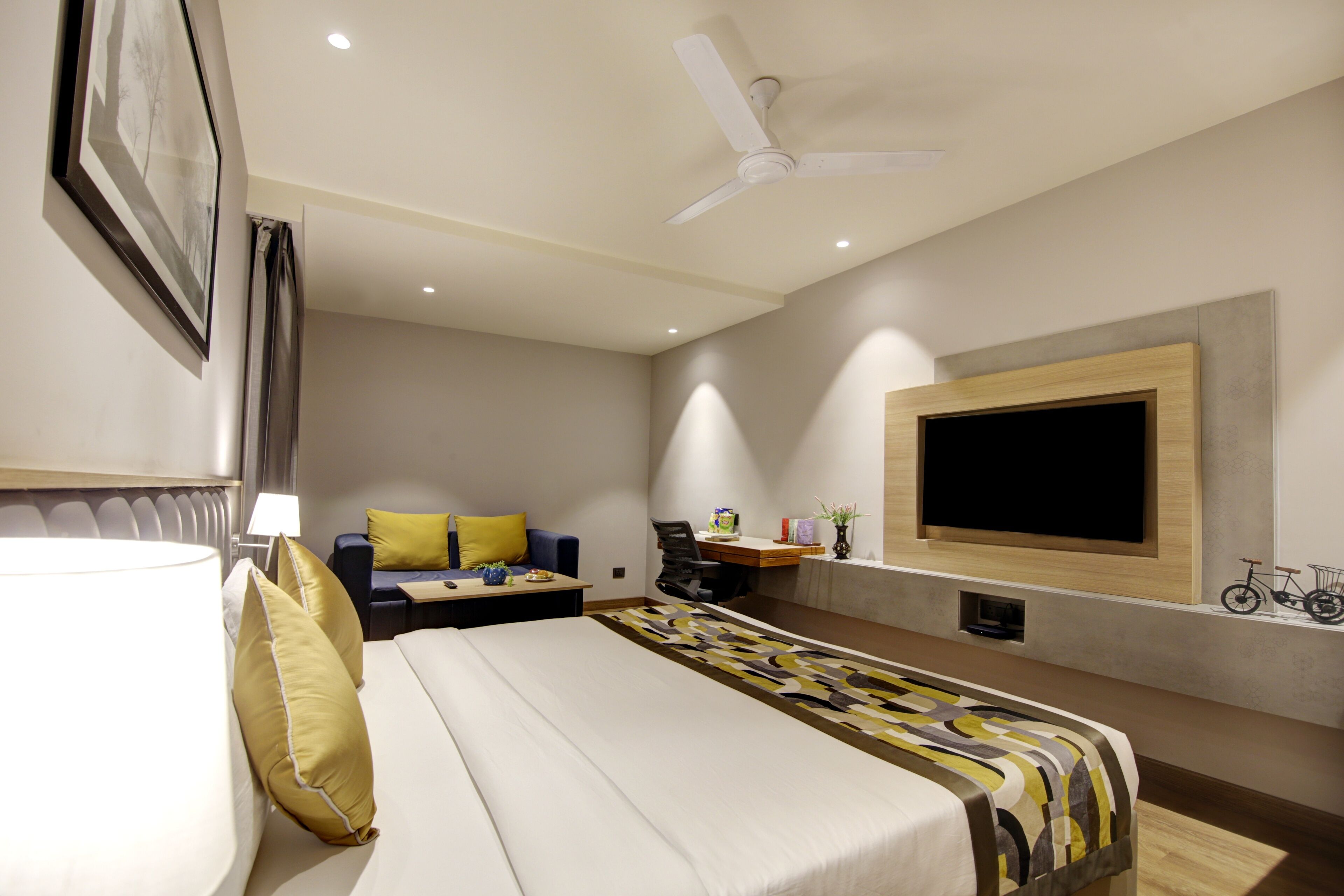 A modern hotel room with a bed, a desk, a chair, a TV, and a ceiling fan.