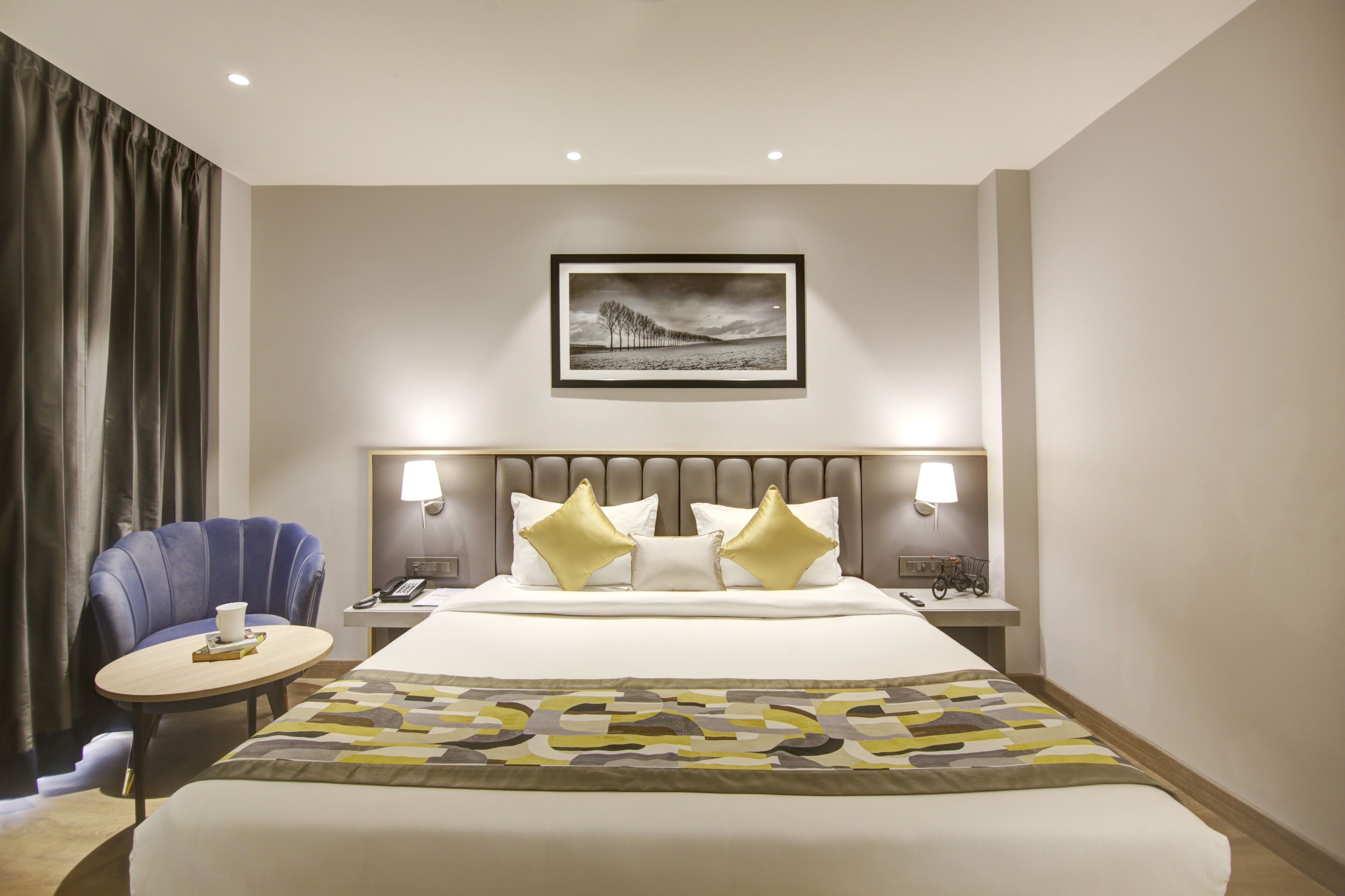 A hotel room with a bed, two bedside lamps, a chair, a small table, and a framed picture on the wall.