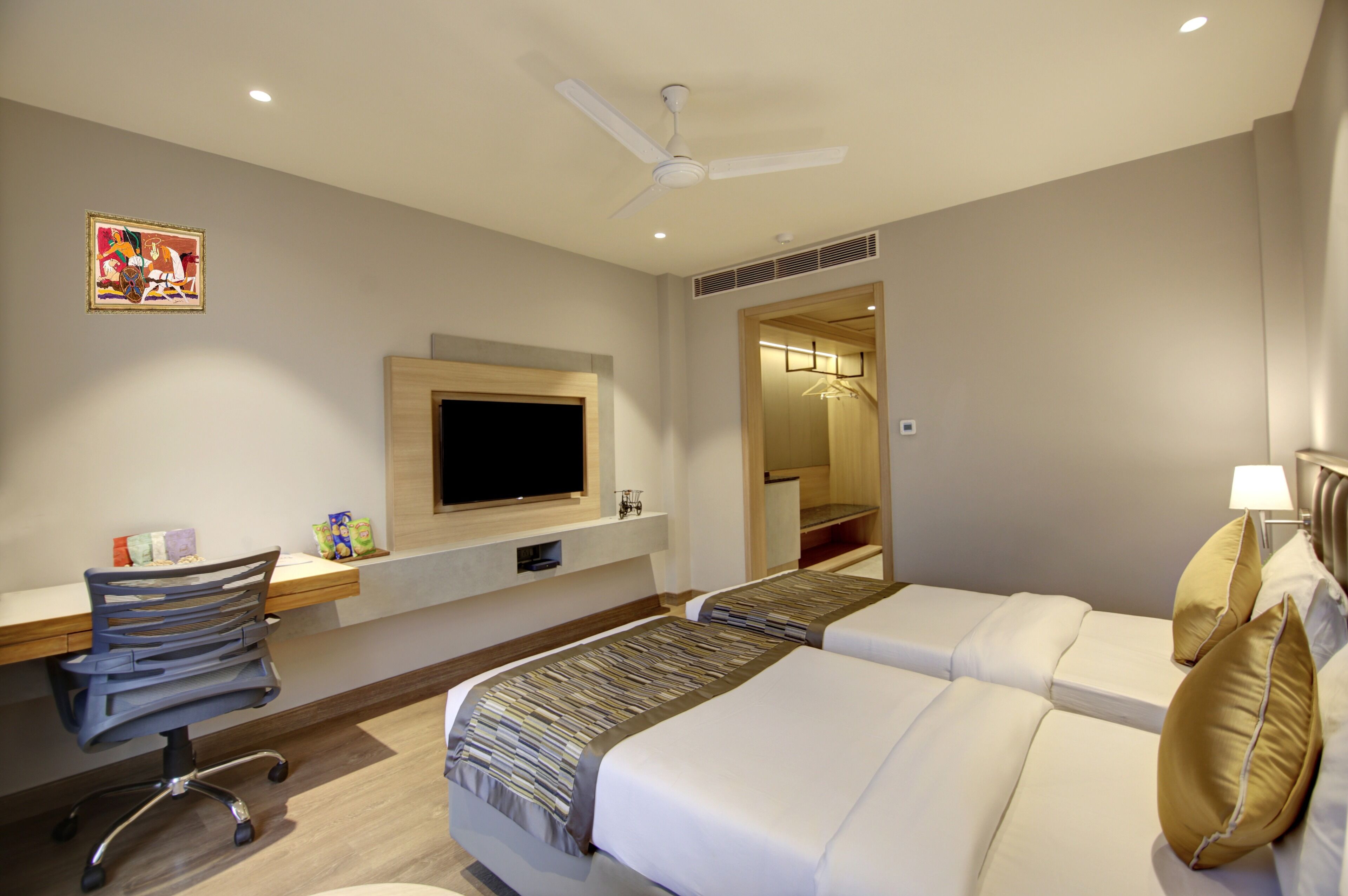 Een hotelkamer met een bed, een bureau met stoel, een televisie en een plafondventilator.