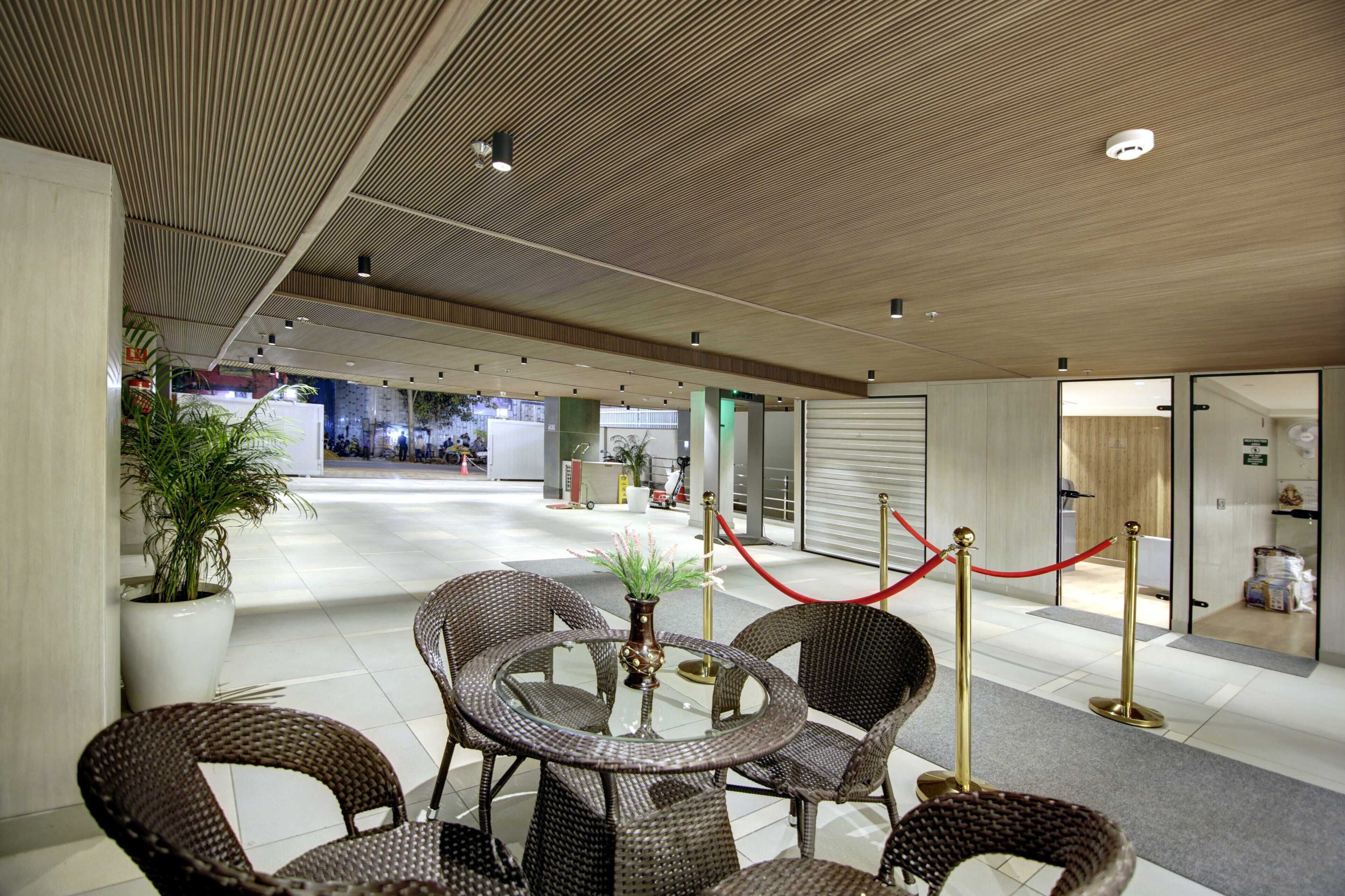 A modern lobby with wicker furniture, a potted plant, and a red rope barrier.